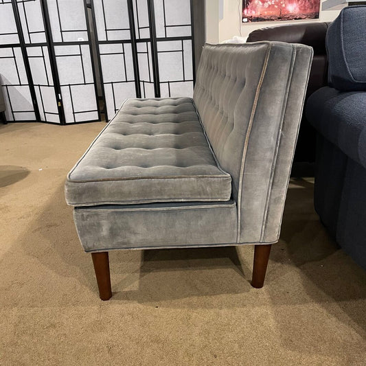 side view of an armless grayish blue sofa on dark wooden legs in a showroom