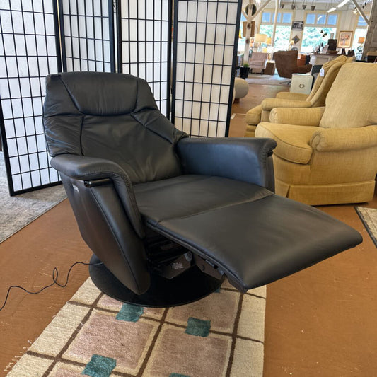 Black leather recliner chair in a showroom setting with other furniture.