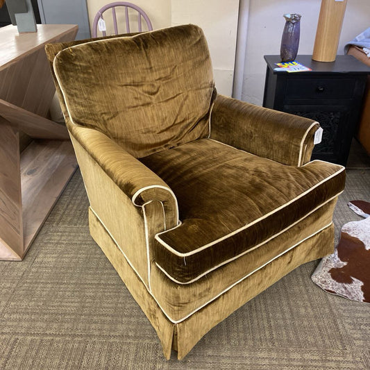 Brown velvet armchair in a room with a desk and chair in the background.