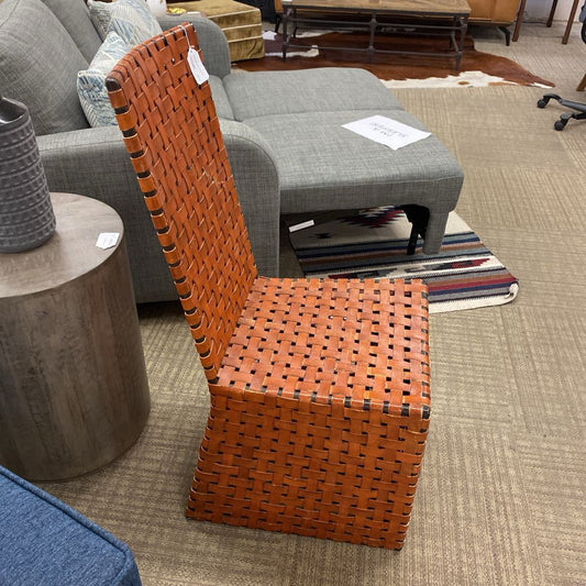Orange woven chair in a furniture store setting with gray sofa and wooden table.