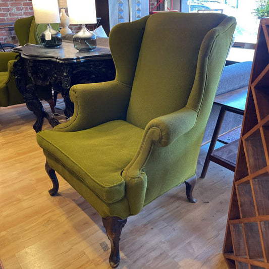 Green wingback chair in a room with wooden floor and furniture.