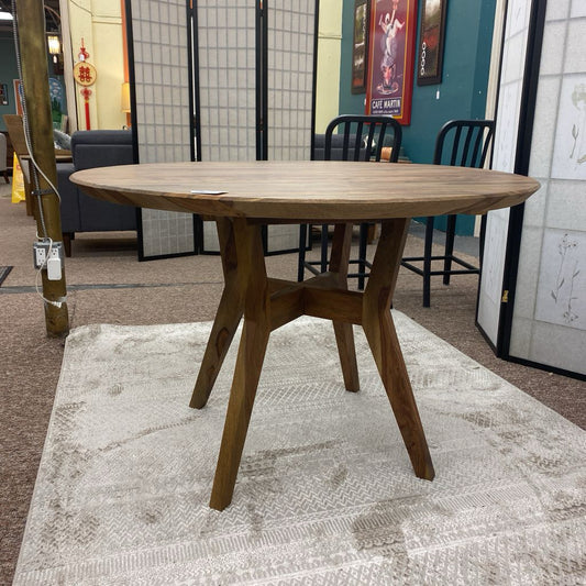 Wooden round table in a showroom setting with chairs and decor elements.