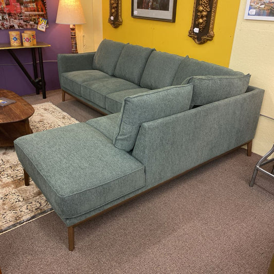 Green sectional sofa in a room with a yellow wall and decorative items.