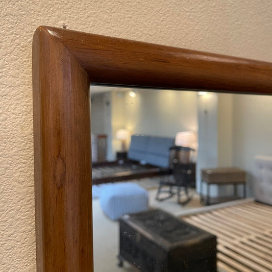 Wooden-framed mirror reflecting a living room with furniture.