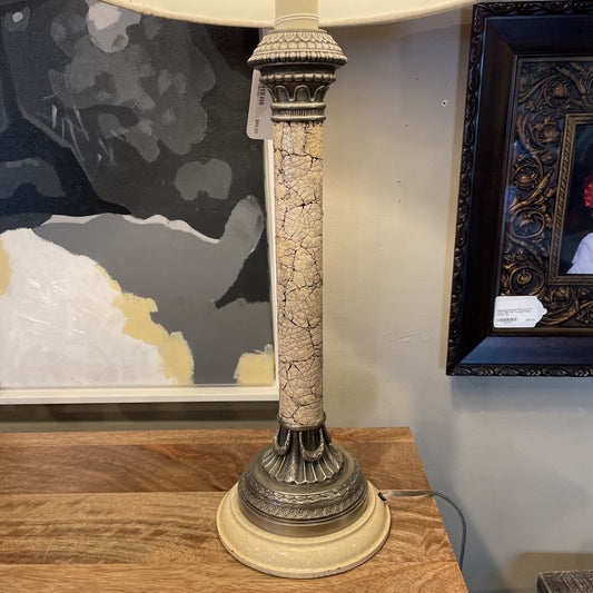 Decorative lamp with a textured base on a wooden surface, with framed artwork in the background.