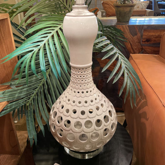 Decorative white lamp with a textured design on a table next to a plant and furniture.