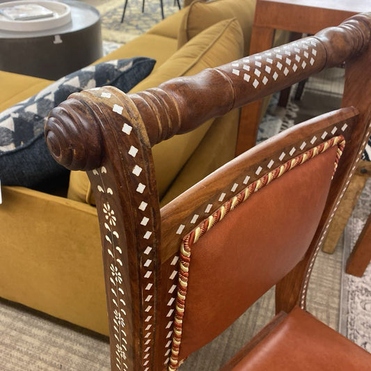 Close-up of a brown leather chair with intricate stitching in a room setting.