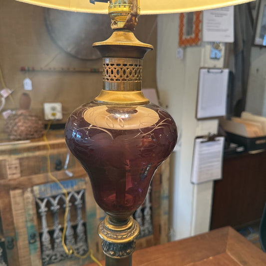 Vintage-style lamp with a red glass base and gold accents on a wooden surface.
