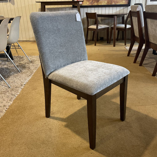 Dining chair with gray cushioned backrest and seat in a showroom setting.