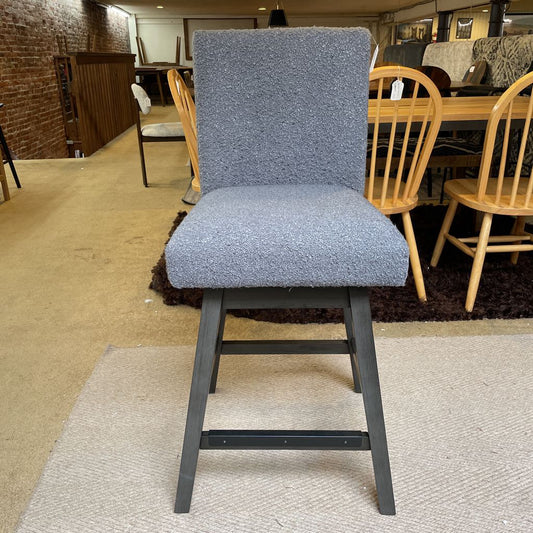 Gray upholstered bar stool with wooden legs in a store setting