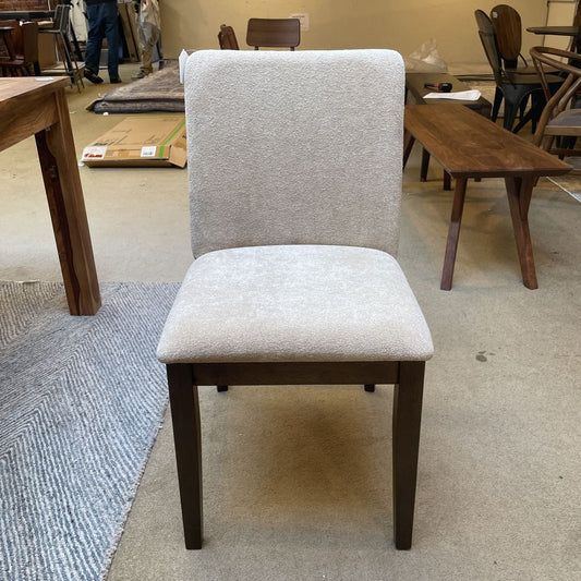 Chair with beige cushioned seat and backrest in a room with tables and chairs.