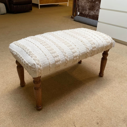 Wooden bench with a textured white cushion on a carpeted floor.