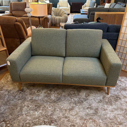 Green sofa in a furniture store setting with other couches and decor items.