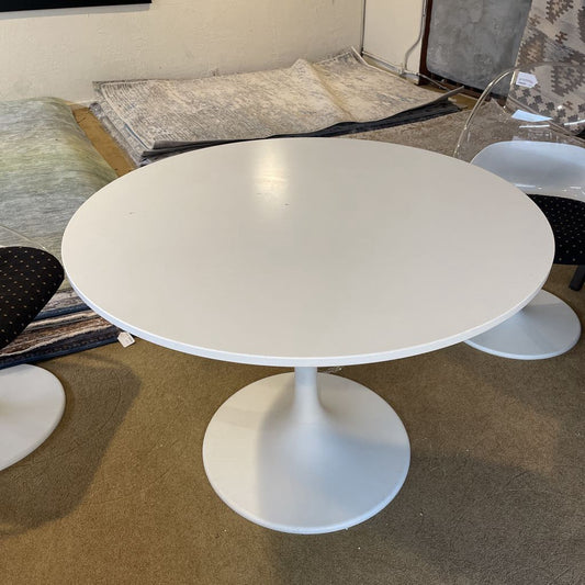 White round table with a pedestal base in a room with patterned rugs and chairs.