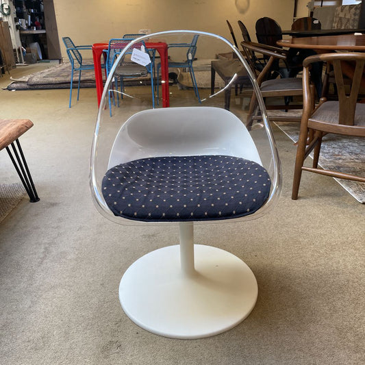 Clear plastic chair with a white base and dark cushion in a room with other furniture.