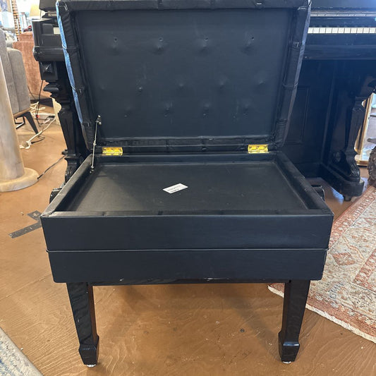 Black piano bench with open lid on a wooden floor