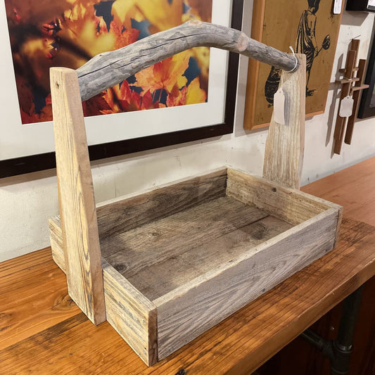 Wooden toolbox with a handle on a wooden surface, with artworks in the background.
