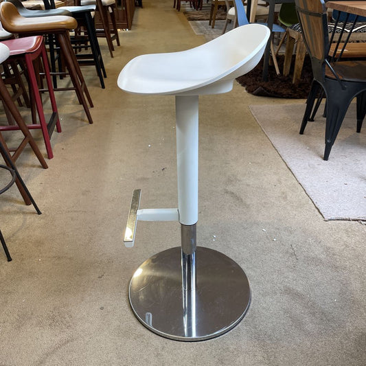 White adjustable bar stool on a concrete floor with chairs and tables in the background
