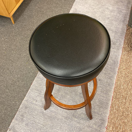 Black cushioned stool with wooden legs on a carpeted floor