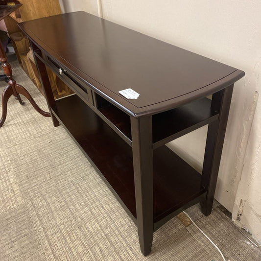 Dark brown wooden table with a shelf on a carpeted floor.