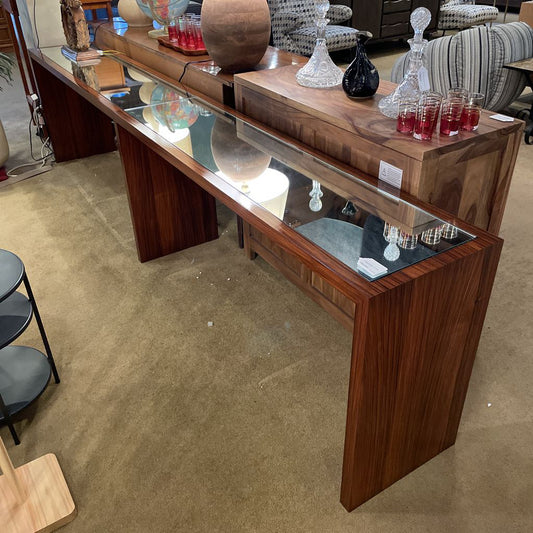 Wooden bar counter with glass top displaying drinks and decor items in a room.