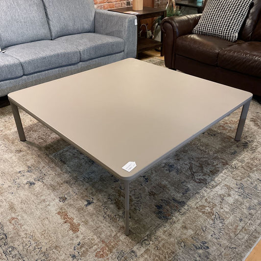 Beige coffee table in a living room setting with gray sofa and brown leather couch.