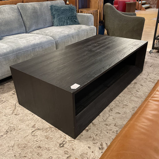 Dark wood coffee table in a living room setting with a gray sofa and brown leather chair.