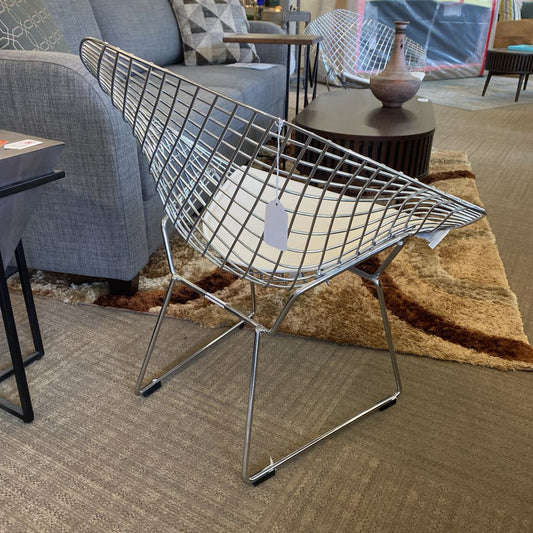 Modern wire chair in a living room setting with a gray sofa and patterned rug.
