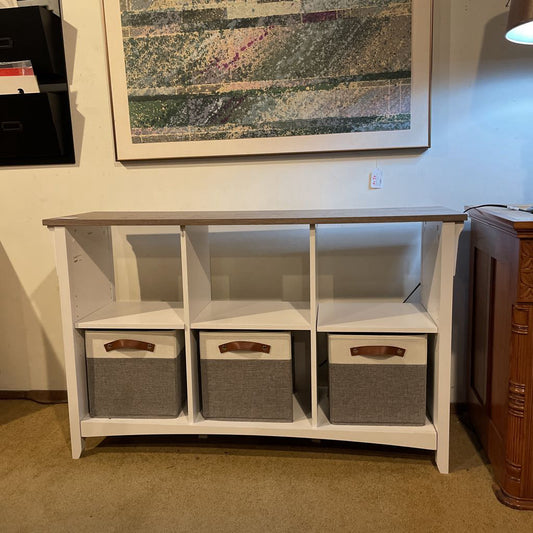 White storage console with three gray baskets underneath, framed artwork on the wall above.