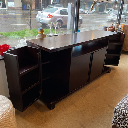 Dark wood office desk with shelves in a room with large windows showing cars outside.