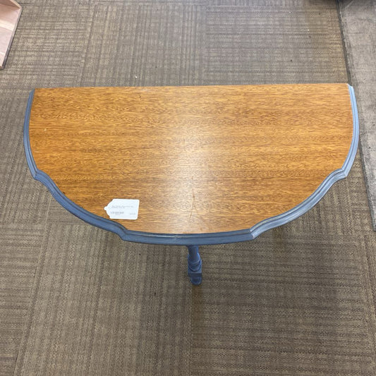 Wooden half-moon table with a blue base on a carpeted floor