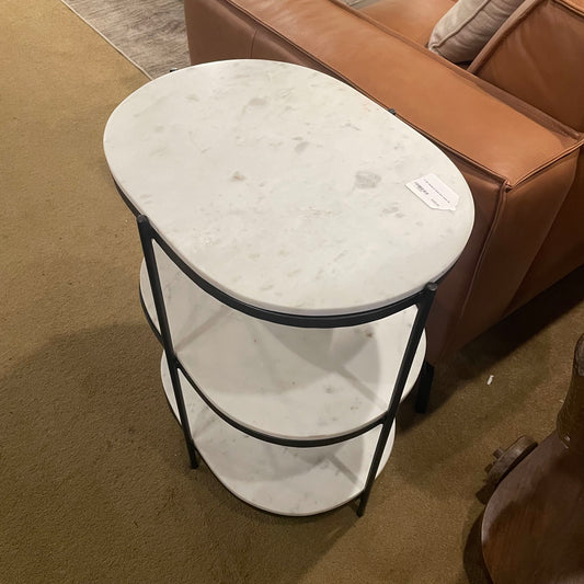 Round marble side table with black metal legs in a living room setting.