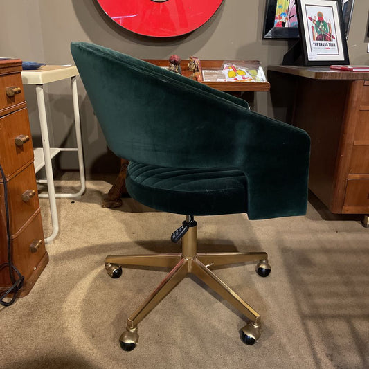 Green office chair with gold base in a room with wooden furniture and a red circular object on the wall.