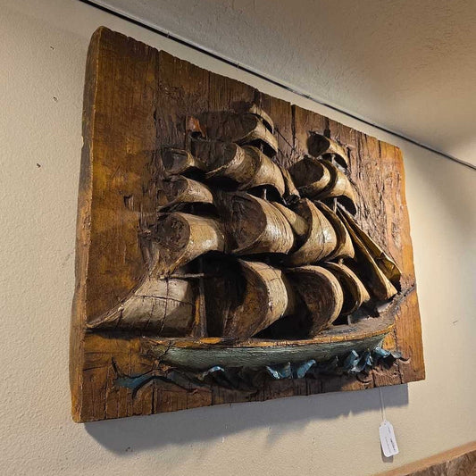 Wooden sculpture of a ship on a wooden base against a beige wall.