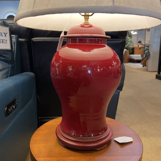 Red ceramic vase with a lampshade on a wooden table in an indoor setting