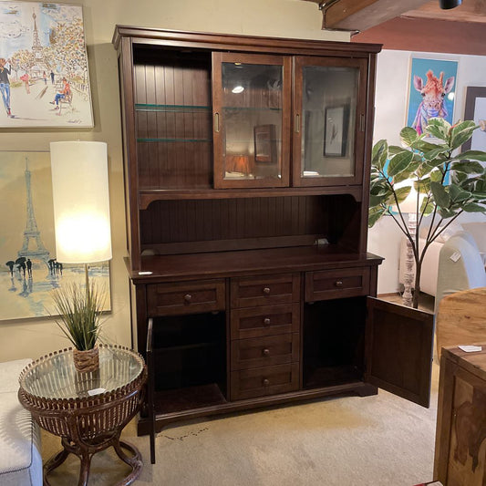Wooden cabinet with glass doors and drawers in a room with paintings and a lamp.