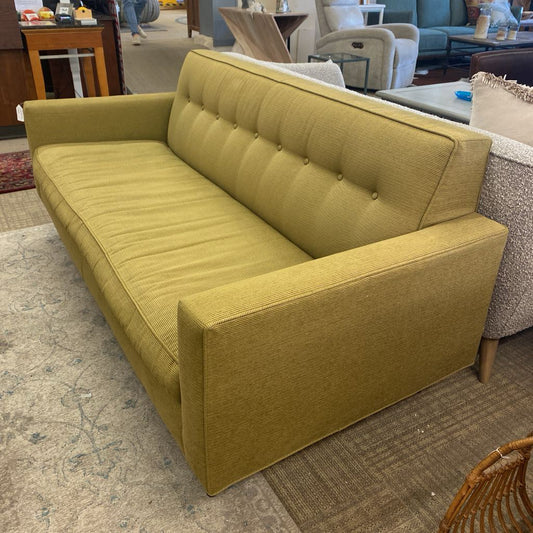 Yellow sofa in a living room setting with other furniture.