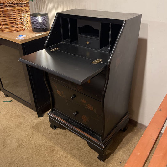 Black wooden desk with open top drawer on a carpeted floor.
