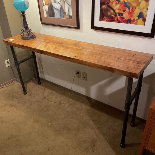 Wooden console table with metal legs against a wall with framed pictures.