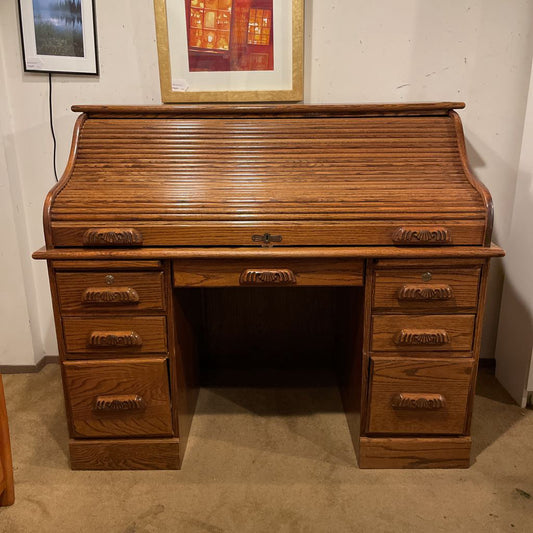 Wooden roll-top desk in a room with framed pictures on the wall.