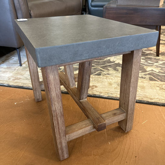 Small side table with concrete top and wooden legs on a wooden floor.