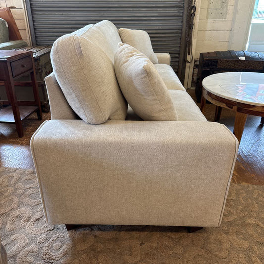 Beige sofa with cushions in a room with wooden furniture and a table.