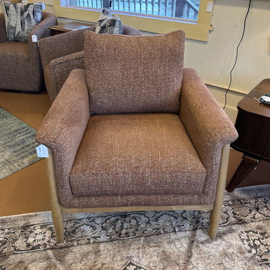 Brown upholstered armchair with a patterned cushion in a room setting.