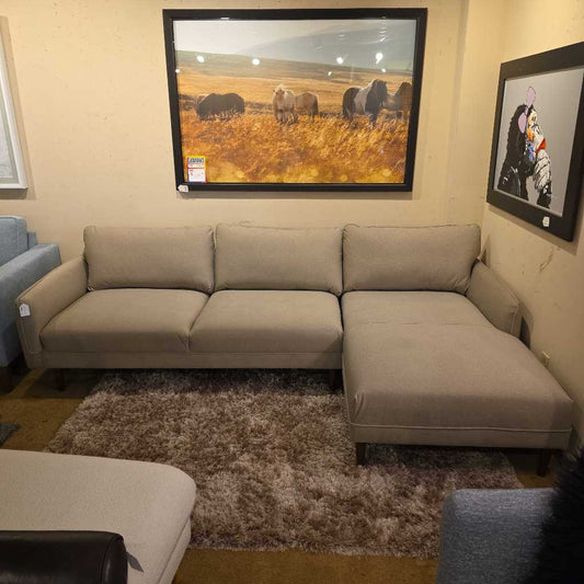 Beige sectional sofa in a room with framed pictures on the wall.