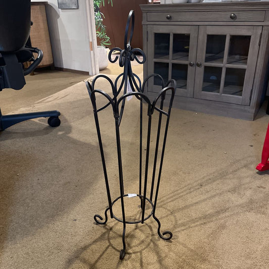 Decorative black metal umbrella stand on a carpeted floor with furniture in the background