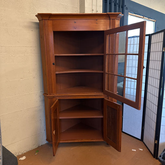 Wooden corner cabinet with glass doors in a room with a tiled floor and white walls.