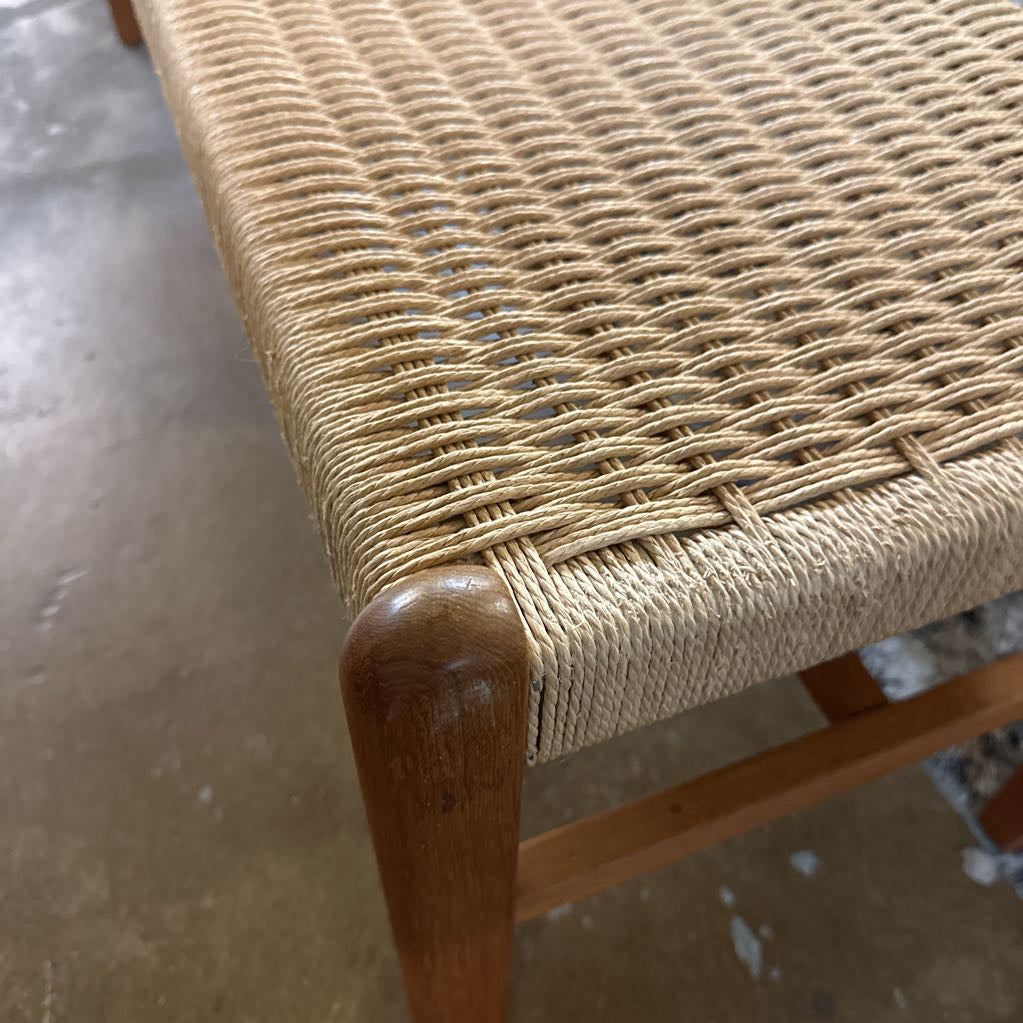 Close-up of a woven chair seat with wooden frame on a concrete floor.