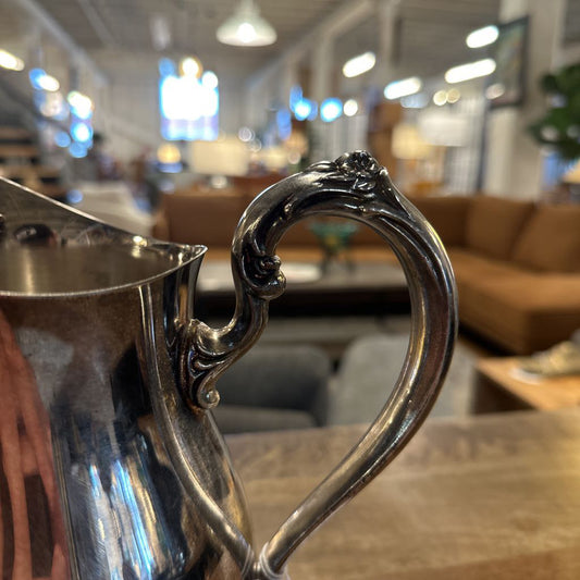 Close-up of a silver pitcher with decorative handle in an indoor setting