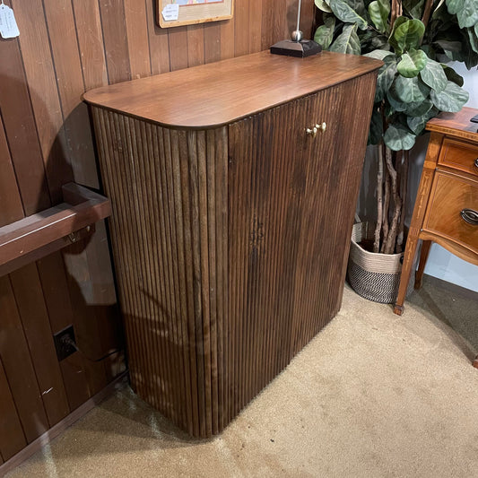 Wooden cabinet with a curved top in a room with wooden walls and a plant.