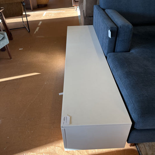 White long box on a brown floor next to a blue sofa